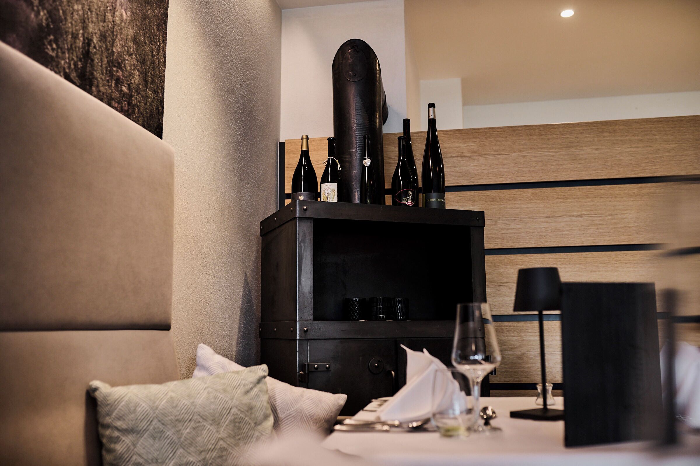 Een eethoek met een bank, een tafel gedekt met een wijnglas, en een kast met wijnflessen.
