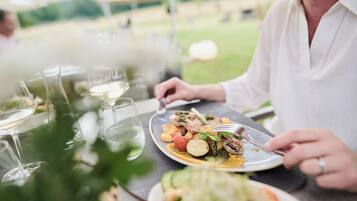 A dining table with plates of food, glasses of white wine, and a person eating.
