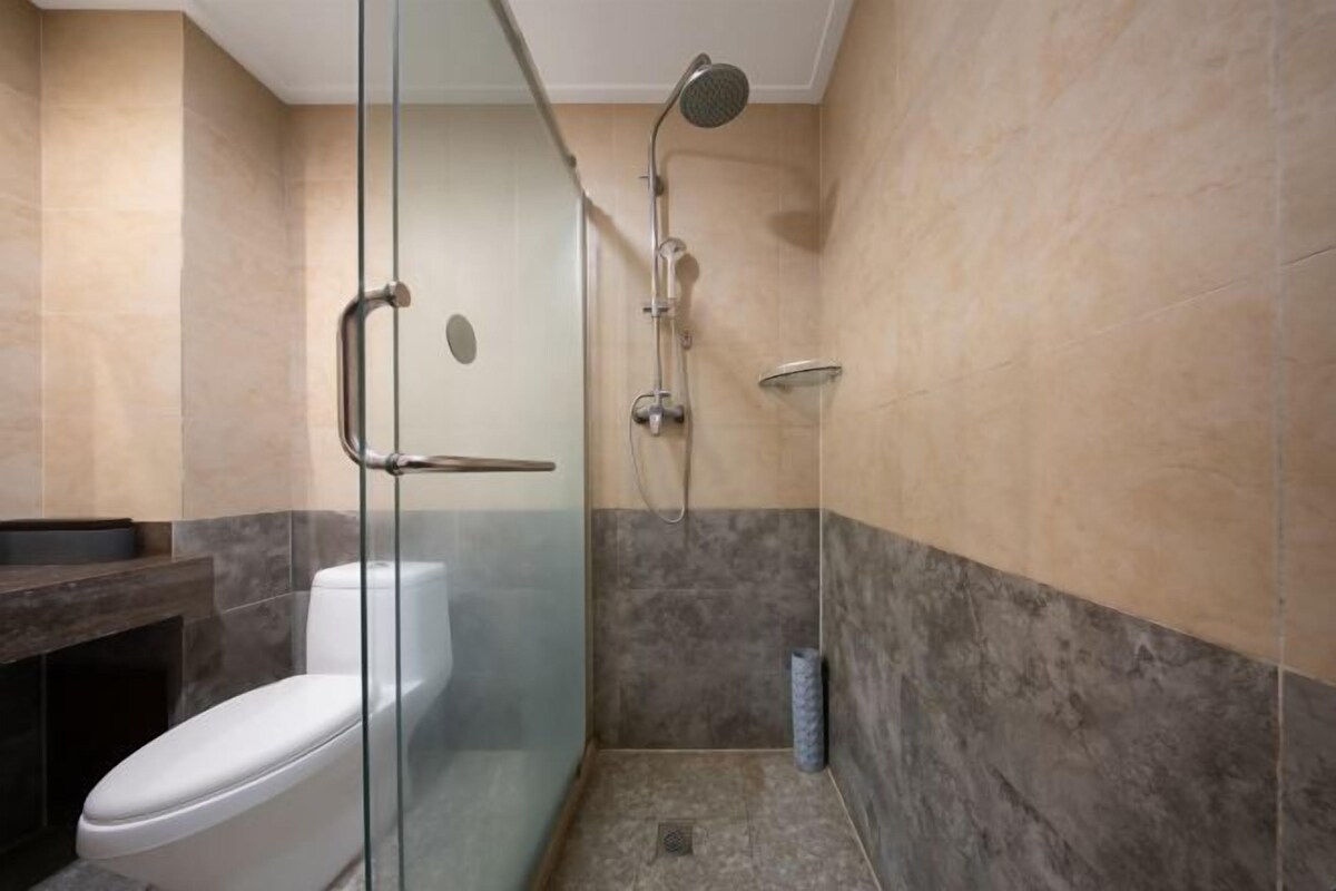 A modern bathroom with a glass-enclosed shower, a toilet, and a marble-tiled wall.