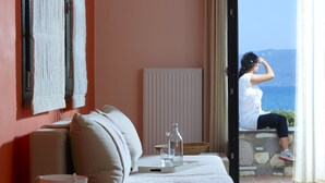 A cozy room with a sofa, a small table with a glass, a vase, and a view of the sea. - Aeolis Apartments & Studios (Lesvos)