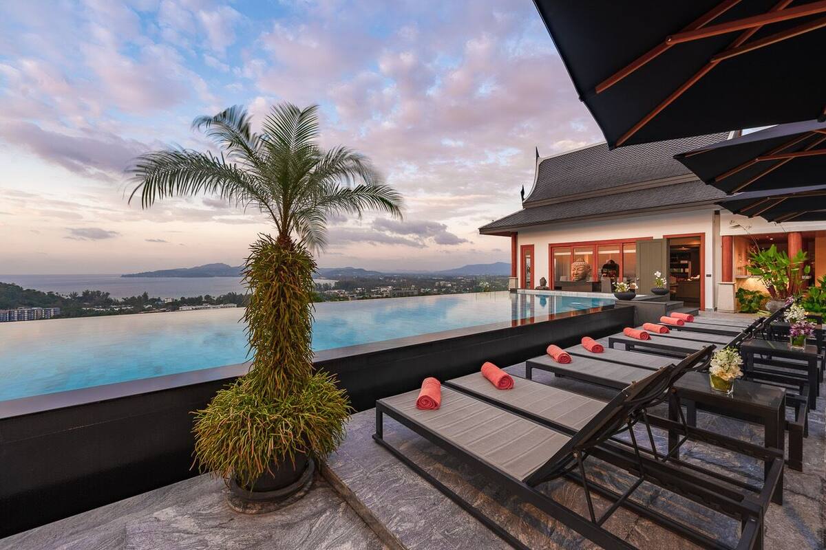 Un área de piscina en la azotea con sillones de descanso y una palmera, con vistas a un paisaje urbano y montañas.