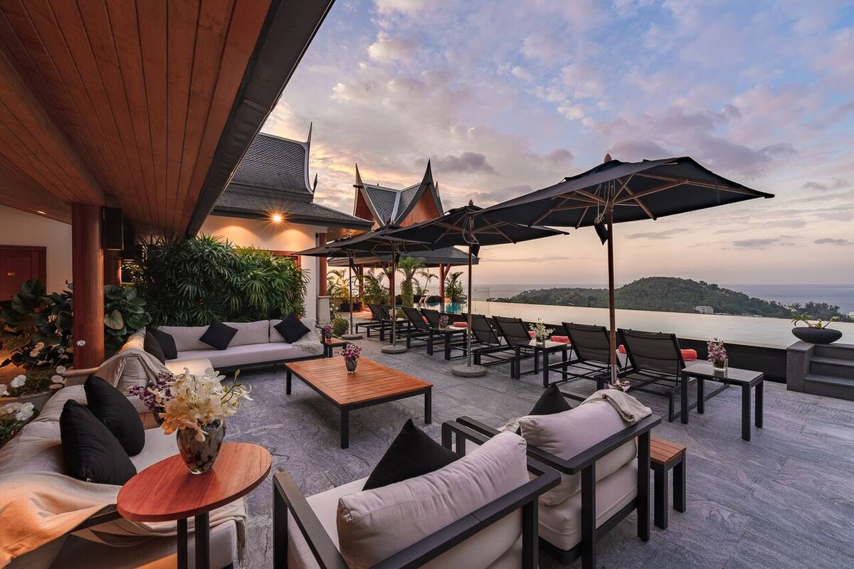 Terraza en la azotea con mobiliario exterior, vista al mar y un edificio tradicional al fondo.