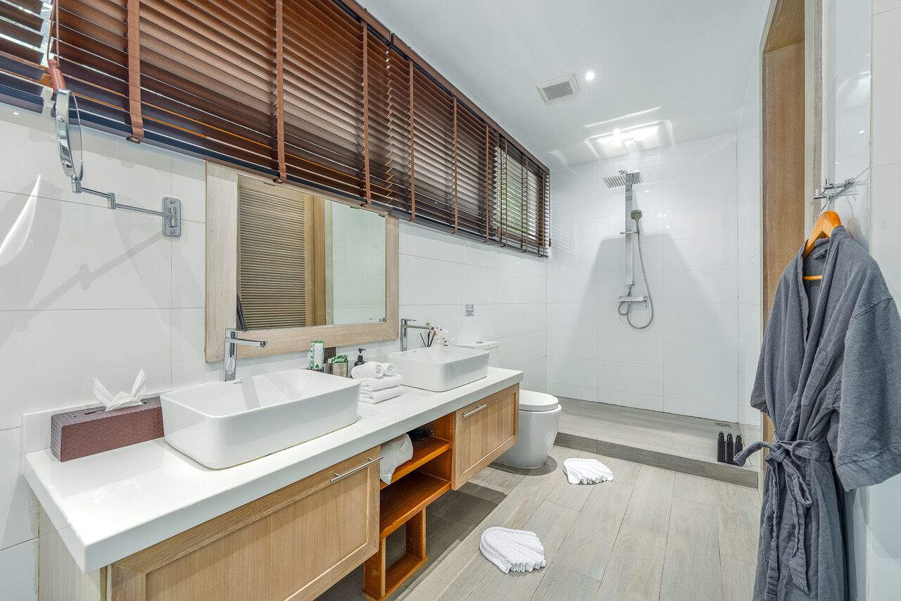 A modern bathroom with two sinks, a large mirror, wooden cabinets, and a shower.