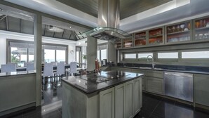 Een moderne keuken met een centraal kookeiland, roestvrijstalen apparatuur en een open kast.