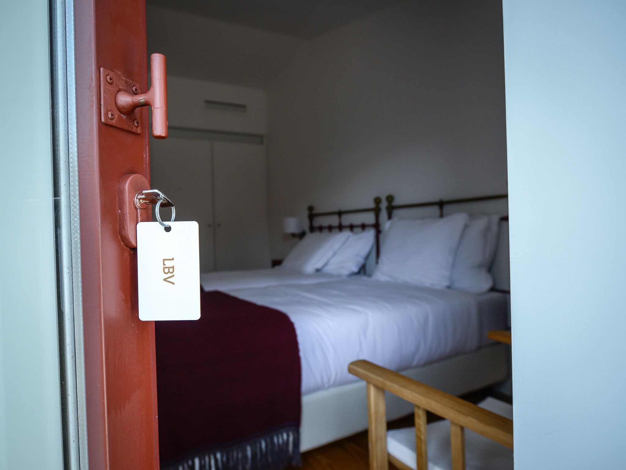 Habitació d'hotel amb un llit, una cadira de fusta i una porta amb lector de targeta.
