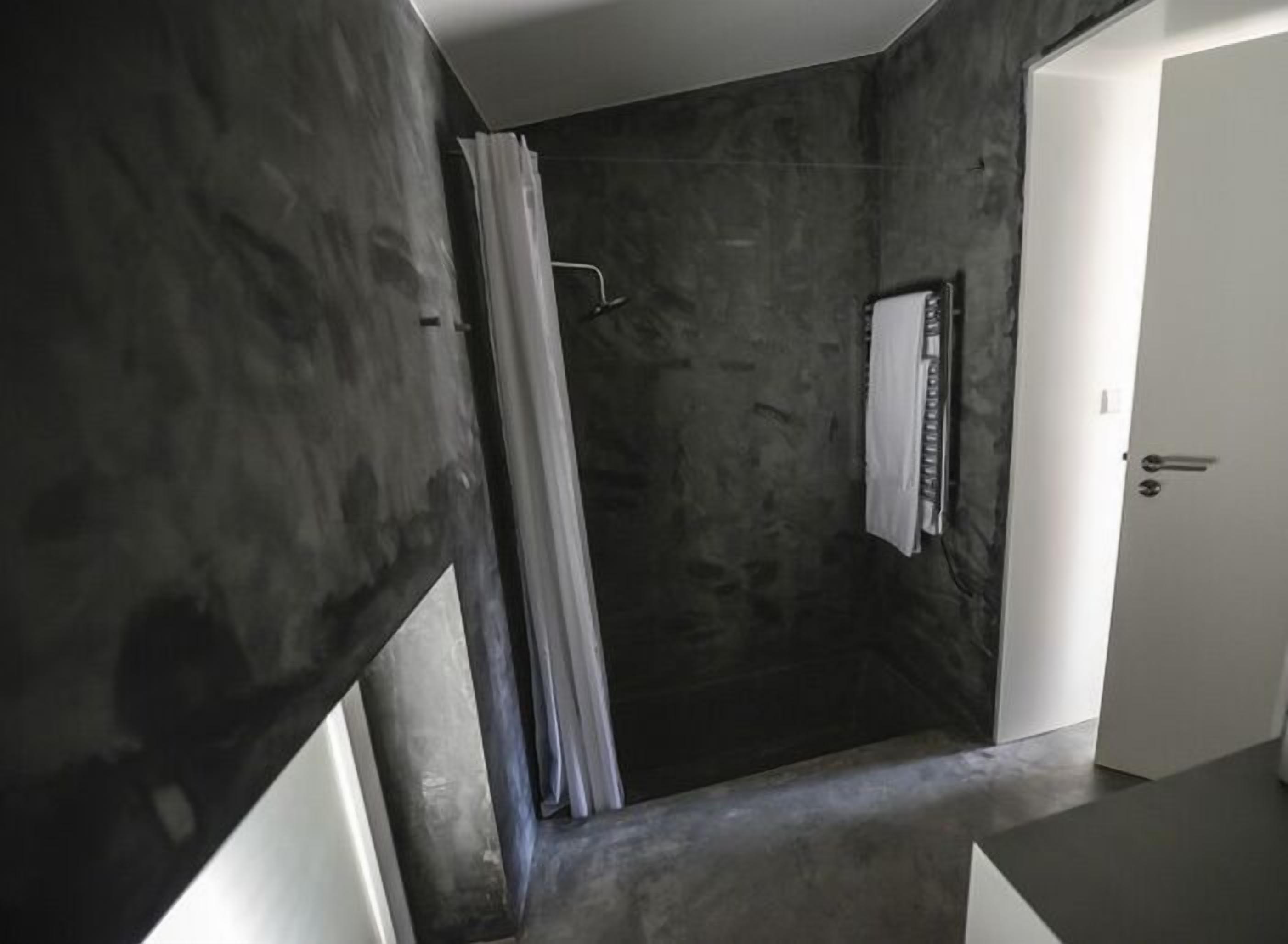Een moderne badkamer met een donkere, gestructureerde wand, een douchegedeelte en een witte deur.