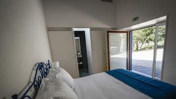 Habitación de hotel con cama, ventana que ofrece vista a follaje y puerta que da a otra habitación.