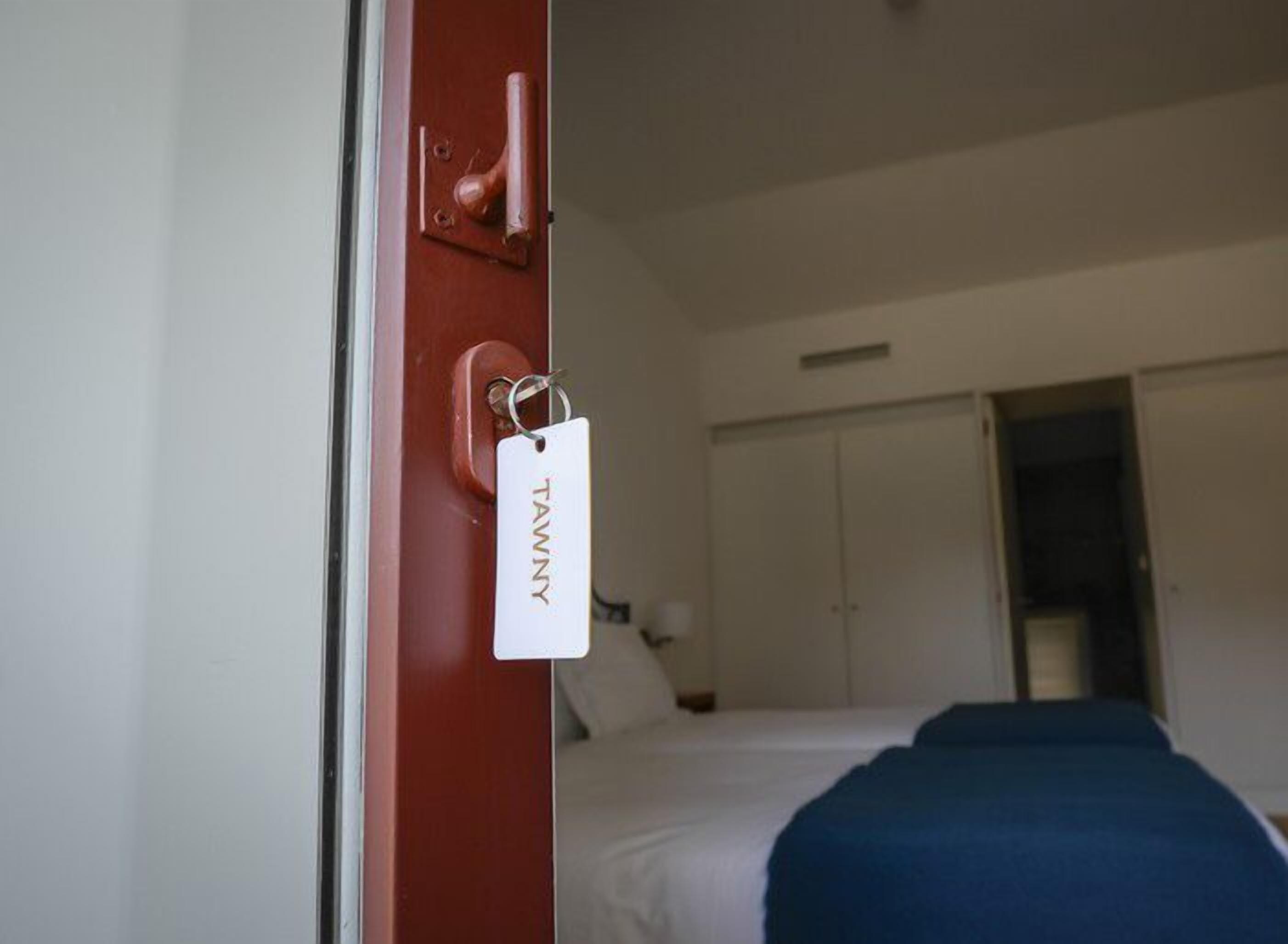 Una camera d'albergo con un letto, un armadio e una porta con un cartellino.