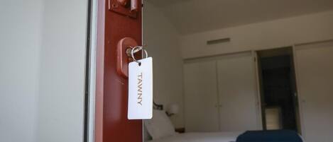 A hotel room with a bed, a wardrobe, and a door with a tag.