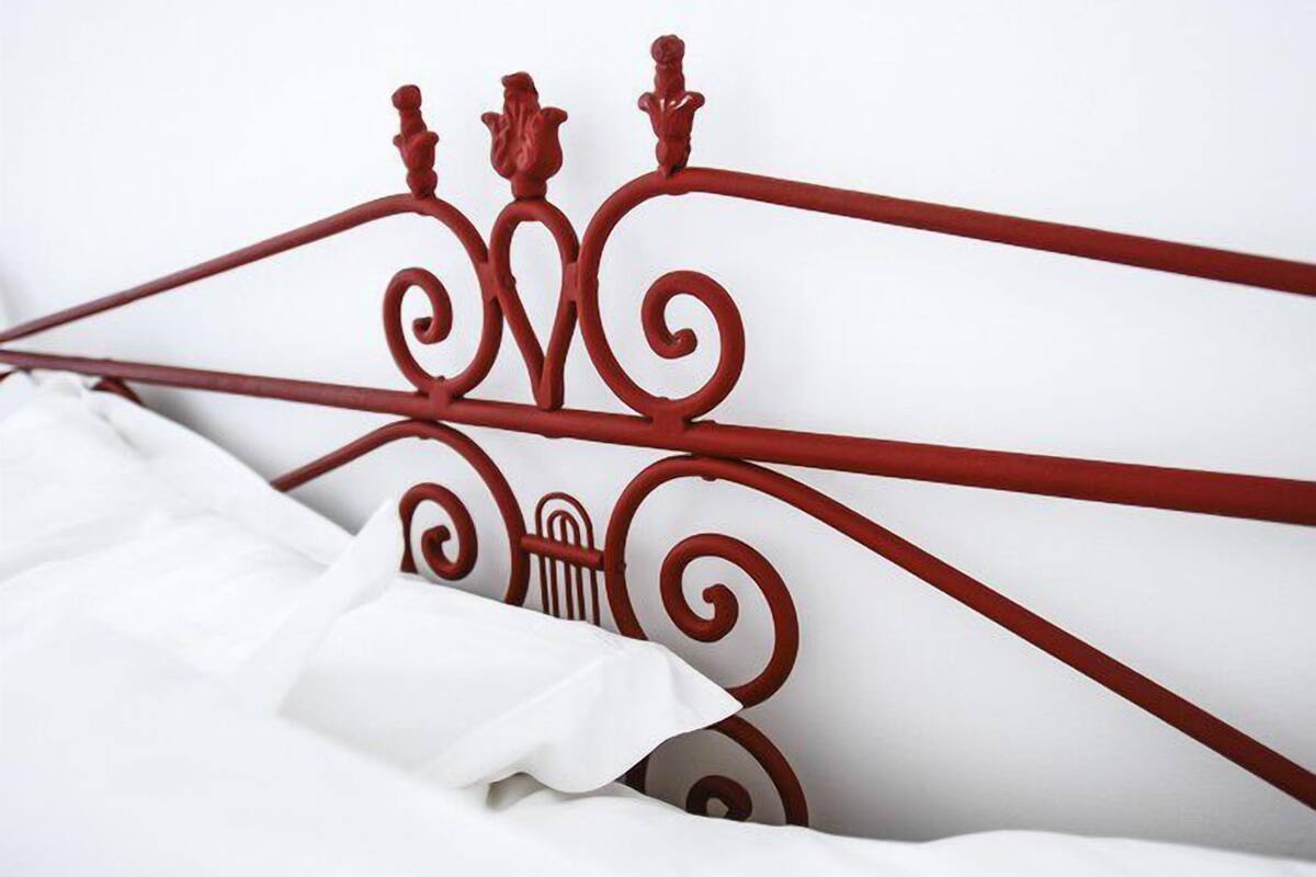A bed with a red metal headboard and white bedding.