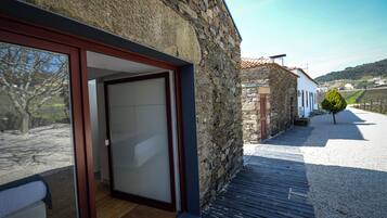 A stone building with a wooden deck and a glass door leading to a room with a bed.