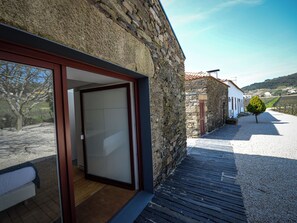 A stone building with a wooden deck and a glass door leading to a room with a bed.