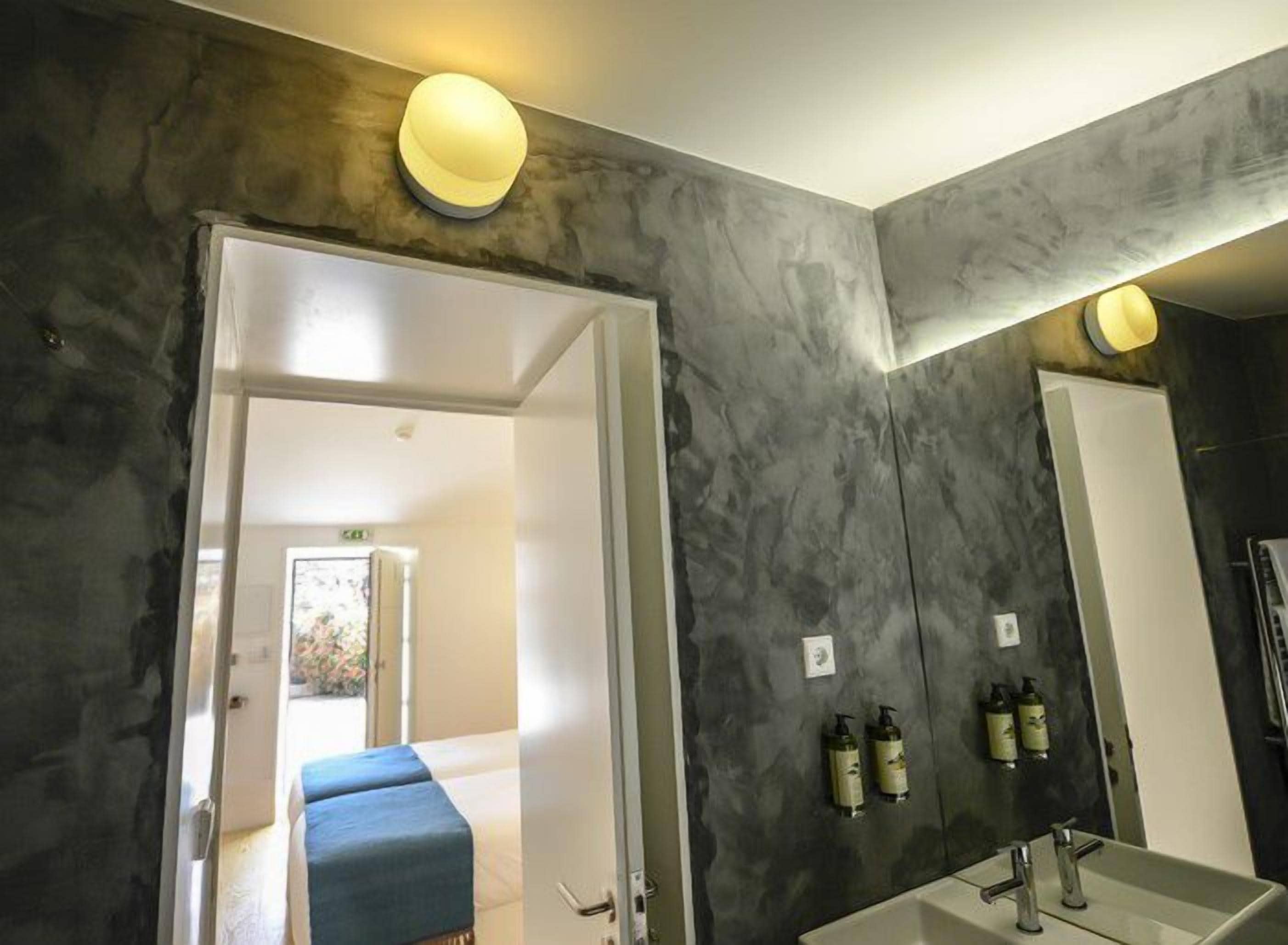 A modern bathroom with a large mirror, a bathtub, and two sinks. There are toiletries on the wall and a door leading to another room.