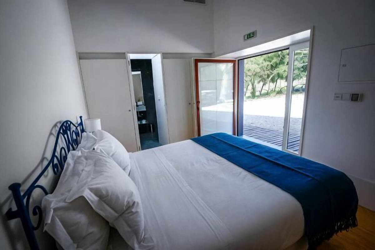 A bedroom with a bed, a window, and a door leading to a balcony.