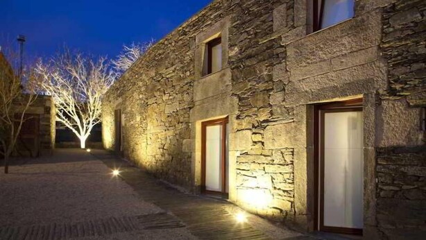 A stone building with two visible doors and a pathway leading to a tree with lights. - Morgadio da Calçada (Sabrosa)