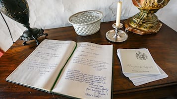 An open notebook with handwritten notes, a candle, a decorative lamp, and a stack of papers on a wooden table.