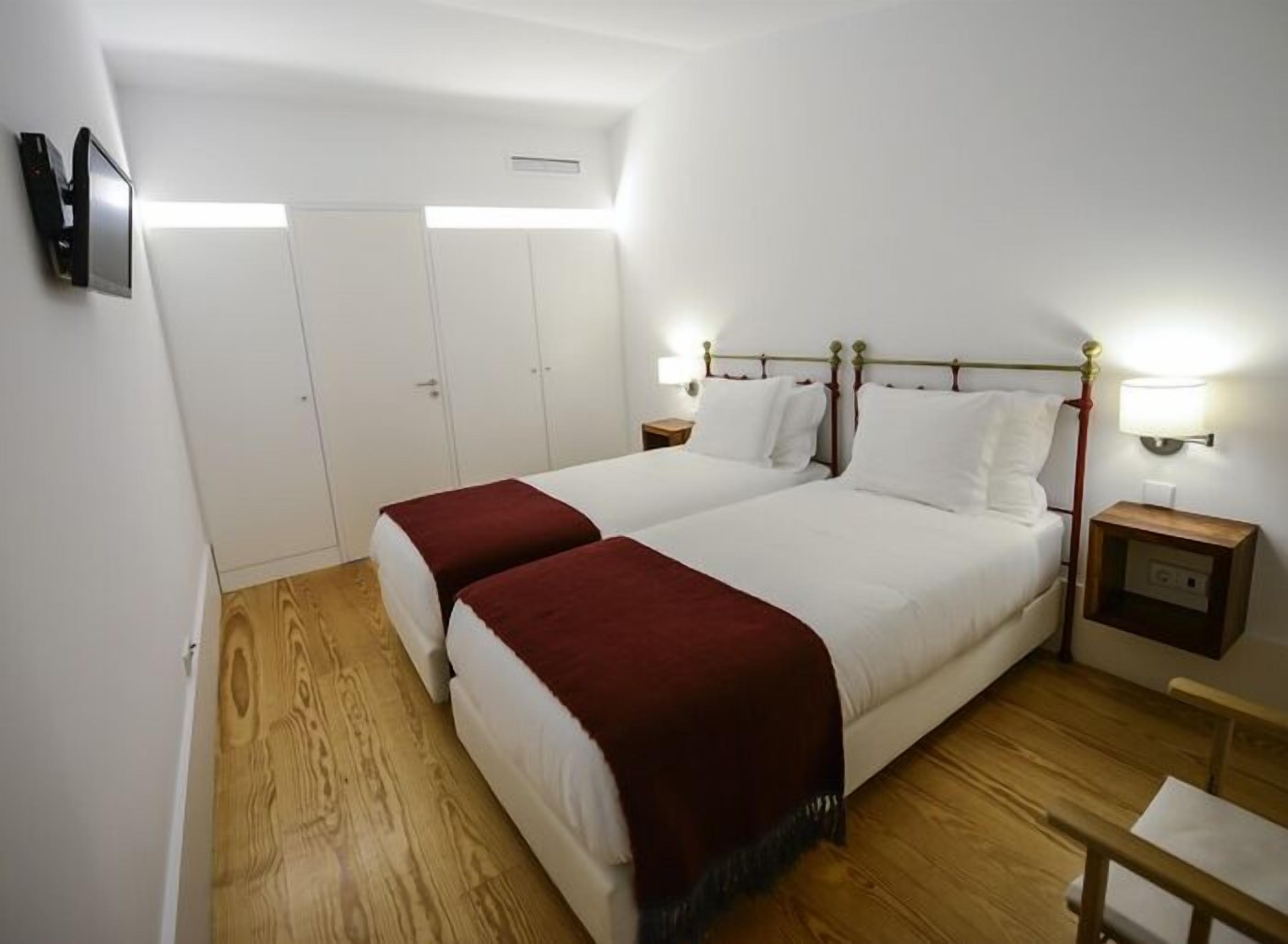 A double bed with a wooden headboard, two bedside tables with lamps, a wooden floor, and a white wardrobe with a mirror.