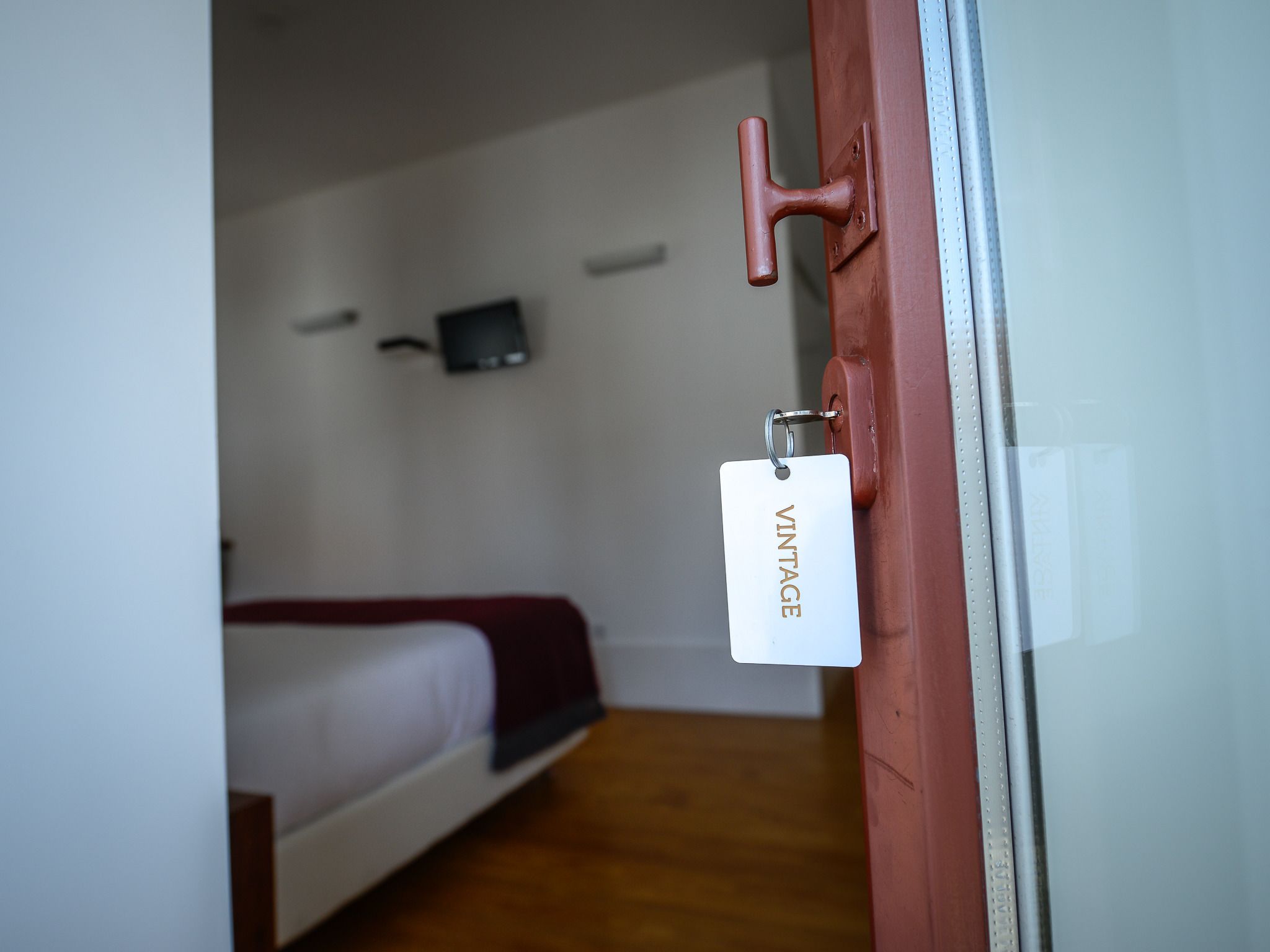 Una habitación con una cama, un televisor montado en la pared y una puerta con una etiqueta antigua.