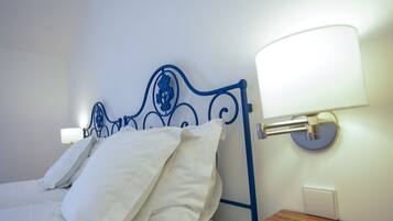A neatly made bed with white linens and pillows, a blue metal headboard, and two wall-mounted lamps on either side.