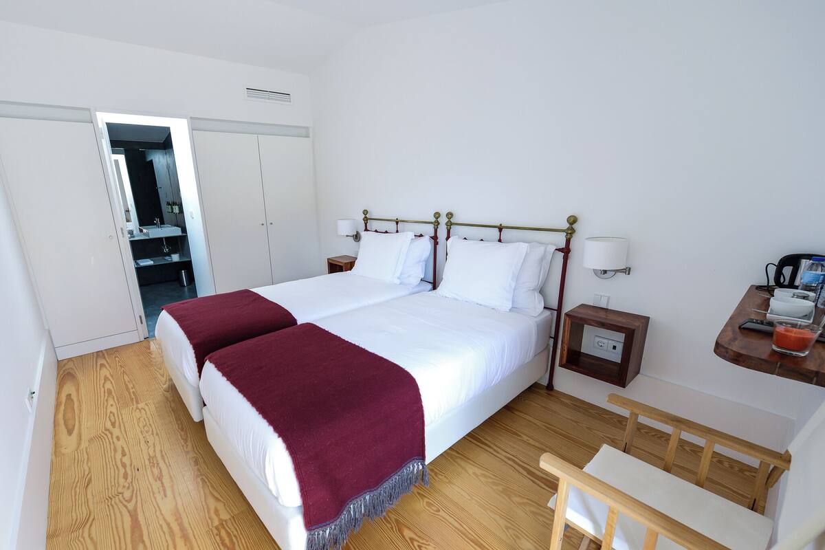 A hotel room with a double bed, two bedside tables, a wooden chair, a small desk, and a wardrobe.