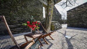 A wooden bench and table set against a stone wall, with a vase of red flowers on the table. - Morgadio da Calçada (Sabrosa)