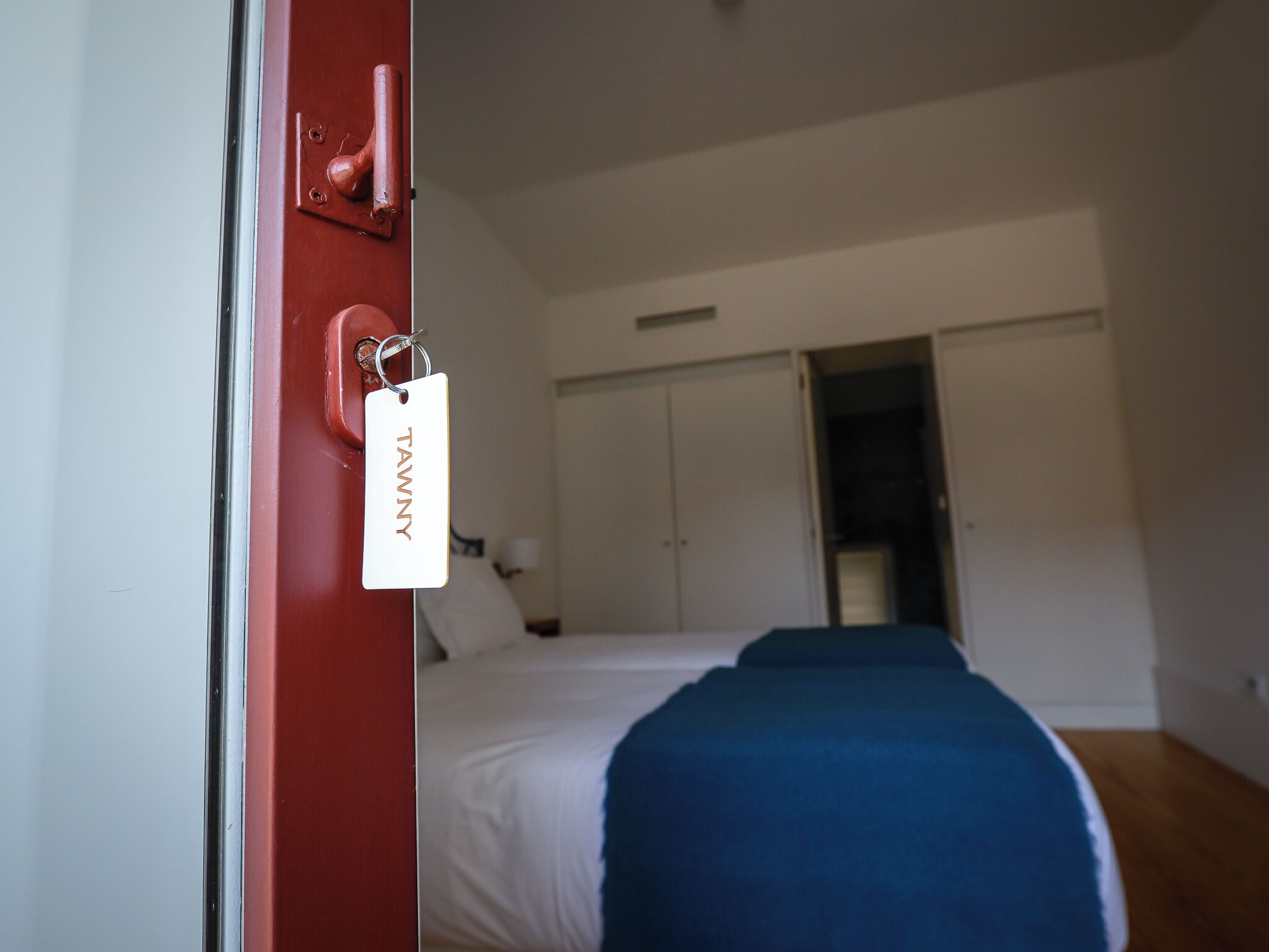 A hotel room with a bed, a wardrobe, and a door with a tag.