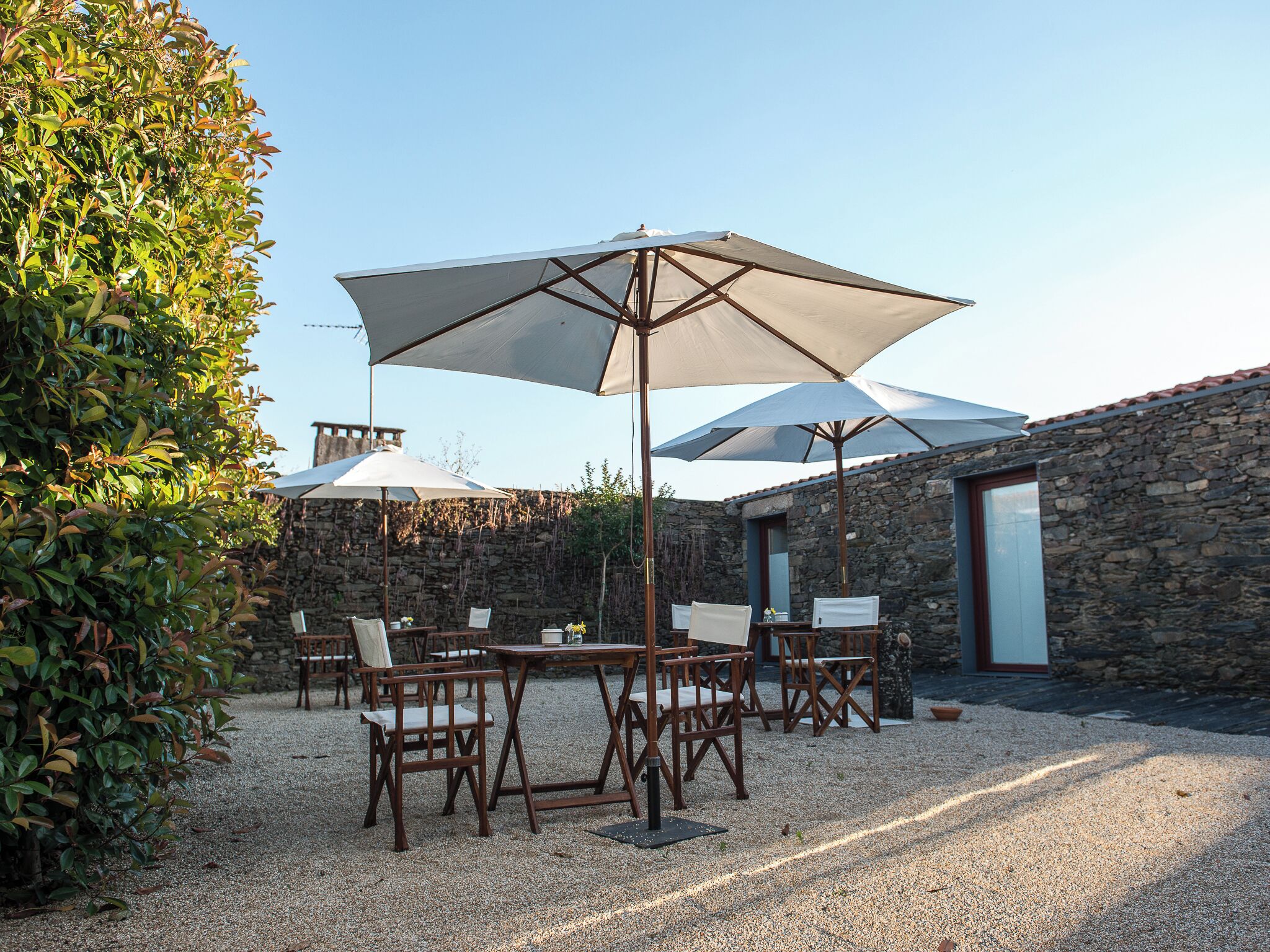 Un espace extérieur aménagé avec des tables et des chaises, protégé du soleil par de grands parasols, le tout adossé à un mur en pierre.