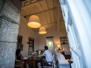 A dining area with a wooden table set for two, a stone wall, and a window with a view of greenery.