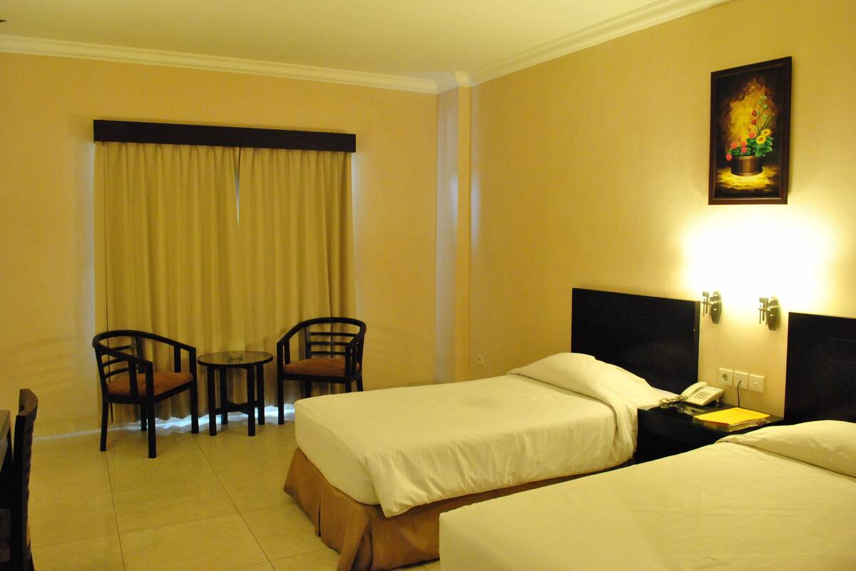 A hotel room with two beds, a desk, two chairs, a painting, and a curtain.