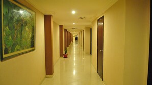 A long, well-lit hallway with doors on one side and a large framed picture on the other.