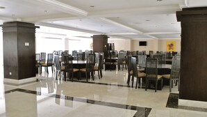 A spacious dining area with multiple tables and chairs, a polished marble floor, and a high ceiling with recessed lighting.