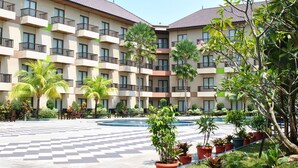 A hotel with multiple balconies, a central pool, and surrounding greenery.