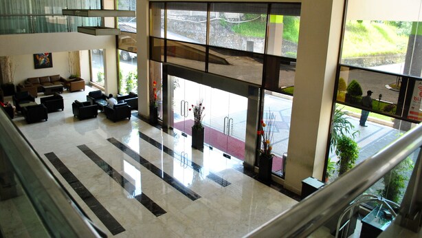 A spacious lobby with a high ceiling, a seating area with sofas and chairs, and large windows offering a view of the outdoors.