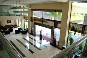 A spacious lobby with a high ceiling, a seating area with sofas and chairs, and large windows offering a view of the outdoors. - Hotel Nuansa Indah (Balikpapan)