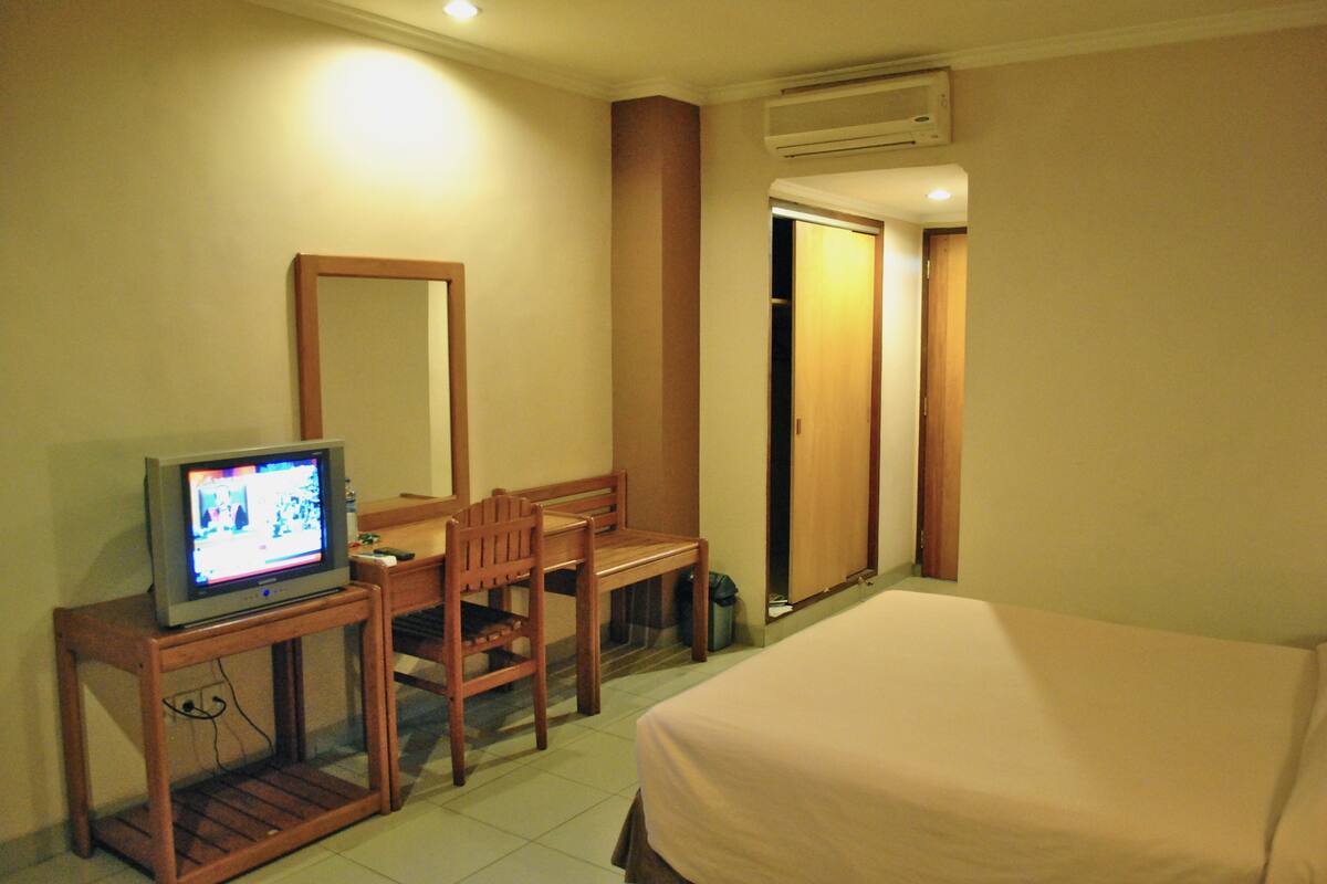 A hotel room with a bed, a desk with a television, a chair, and a mirror.