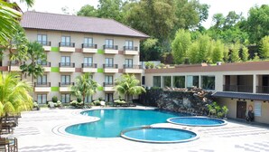 A hotel with multiple swimming pools, outdoor seating, and a lush green environment.