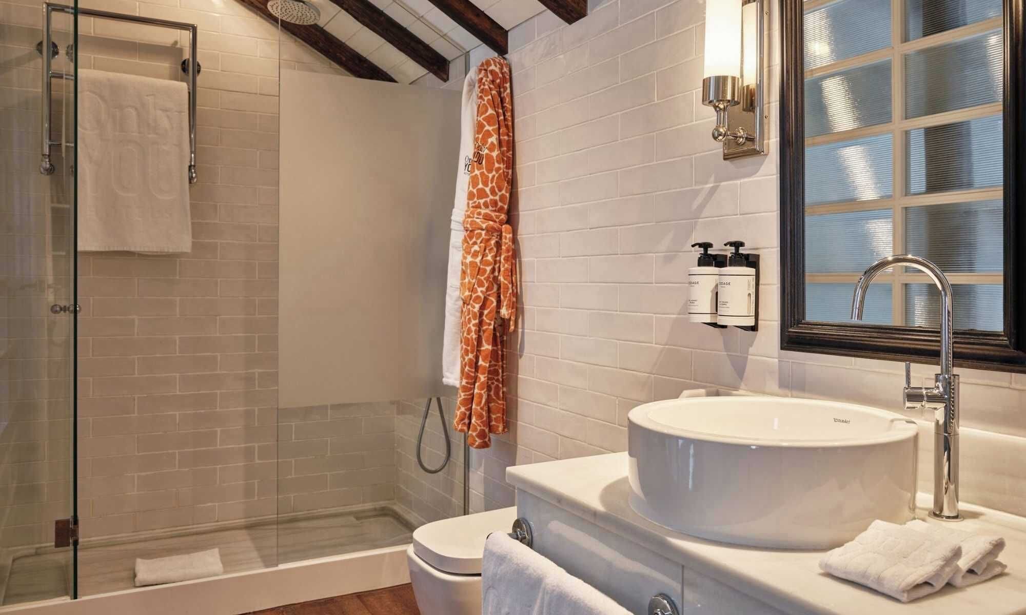 Un baño con cabina de ducha de vidrio, un lavabo blanco con una pileta grande y una ventana con persianas.