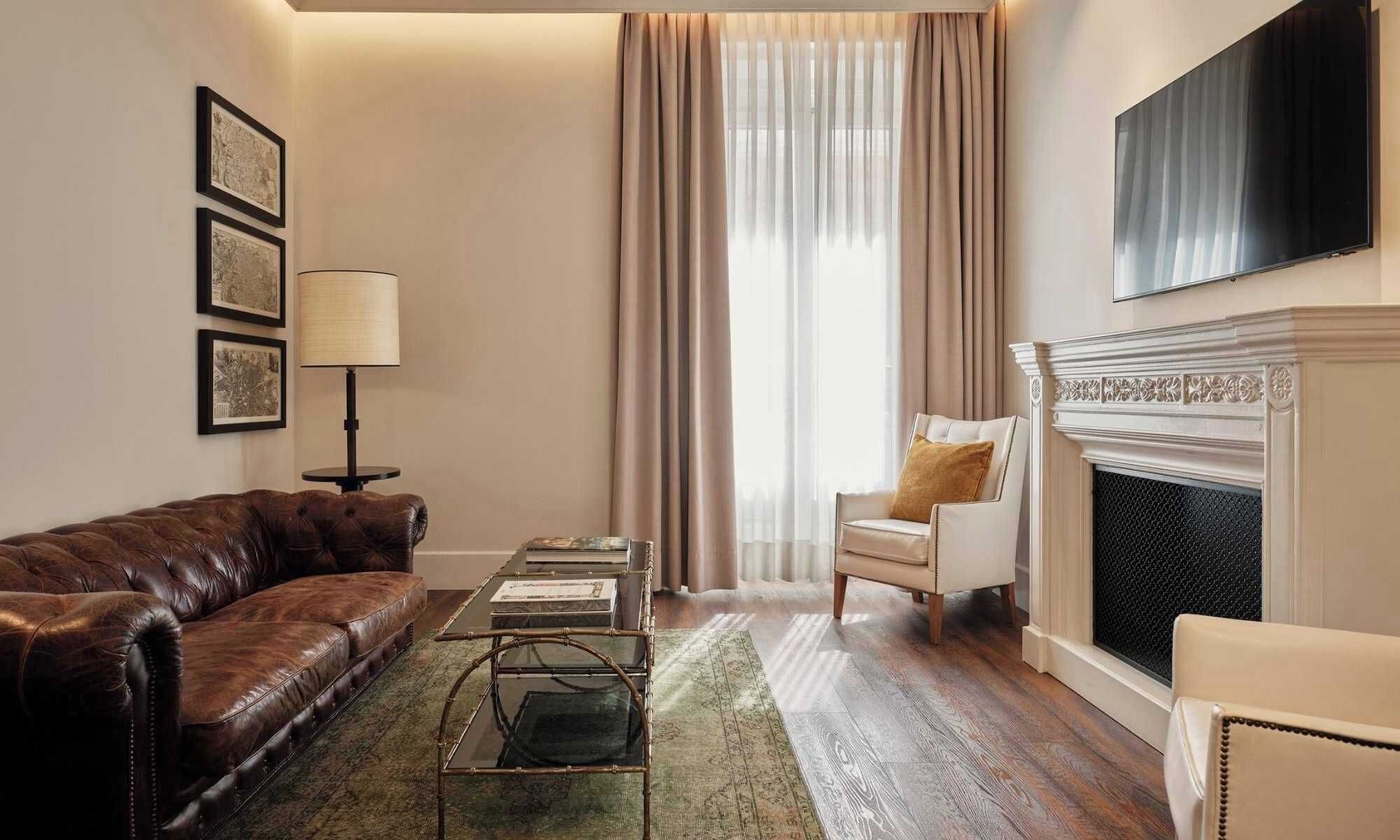 A living room with a brown leather sofa, a glass coffee table, a white armchair, a fireplace, and a television mounted on the wall.