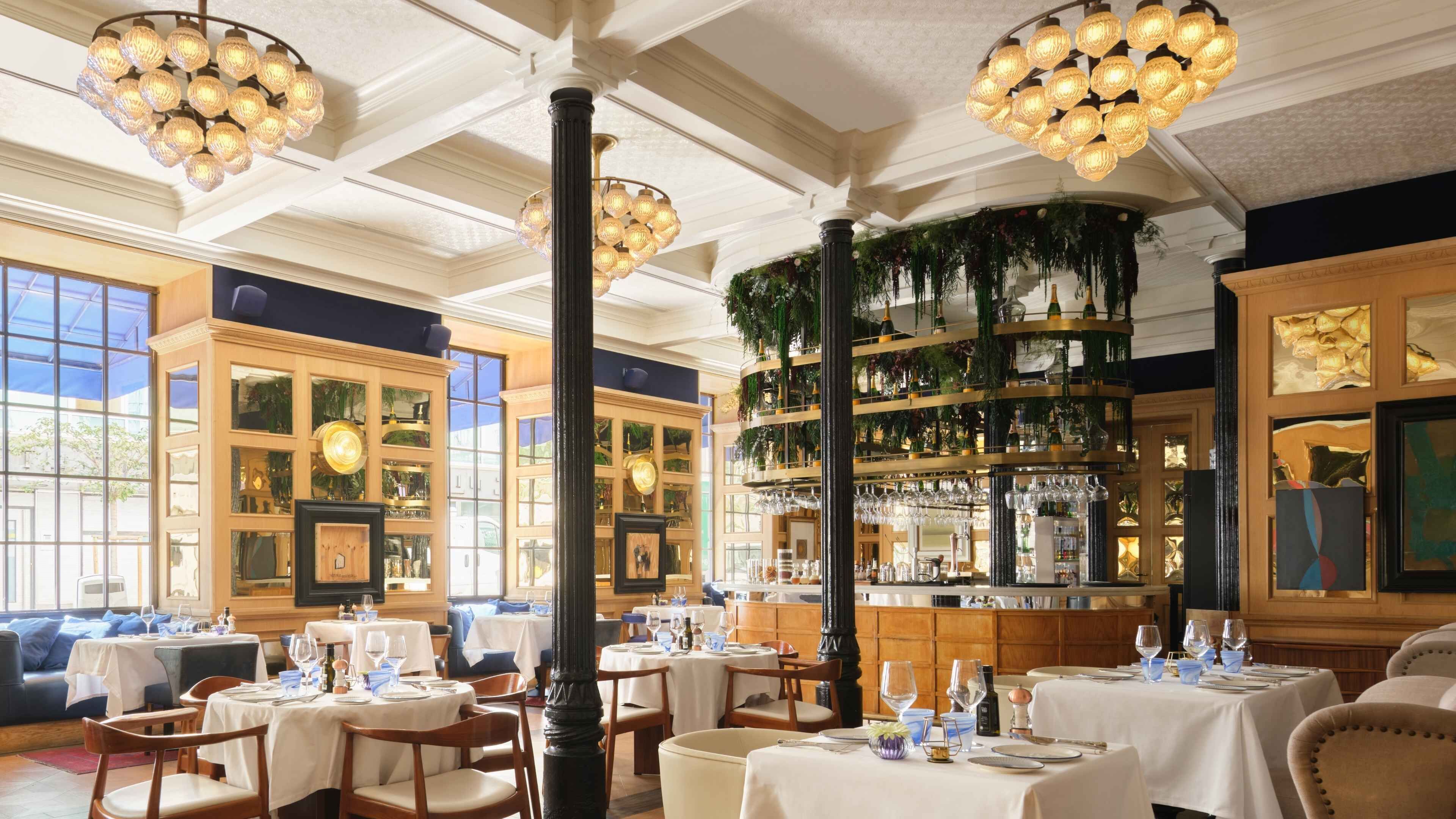 A restaurant with multiple tables, a bar area, and large windows.