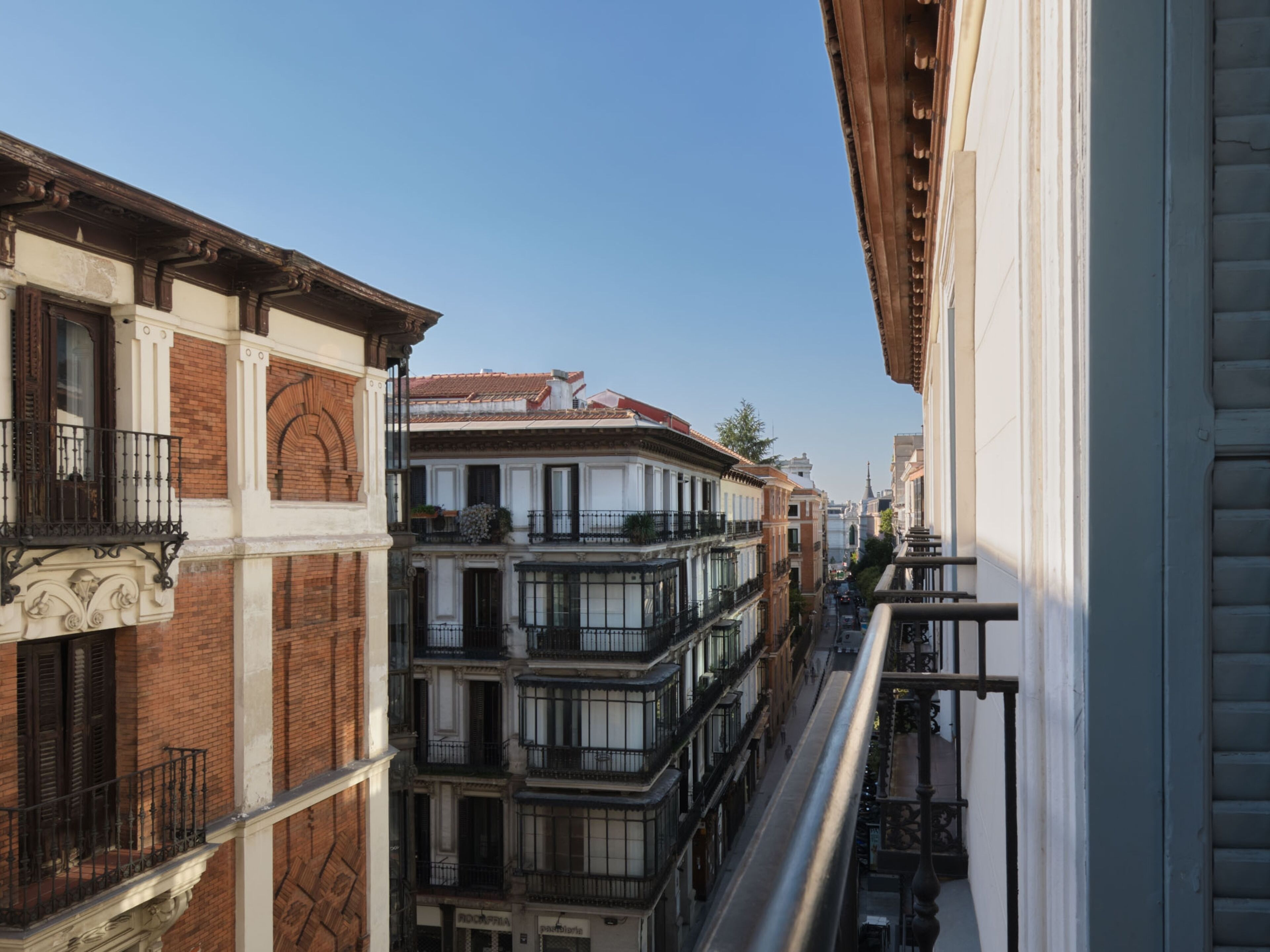 A narrow street flanked by multi-story buildings with balconies and a clear sky.