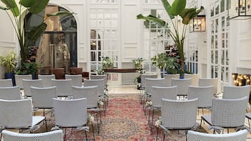 A formal indoor setting with rows of checkered chairs, a central aisle, and potted plants.