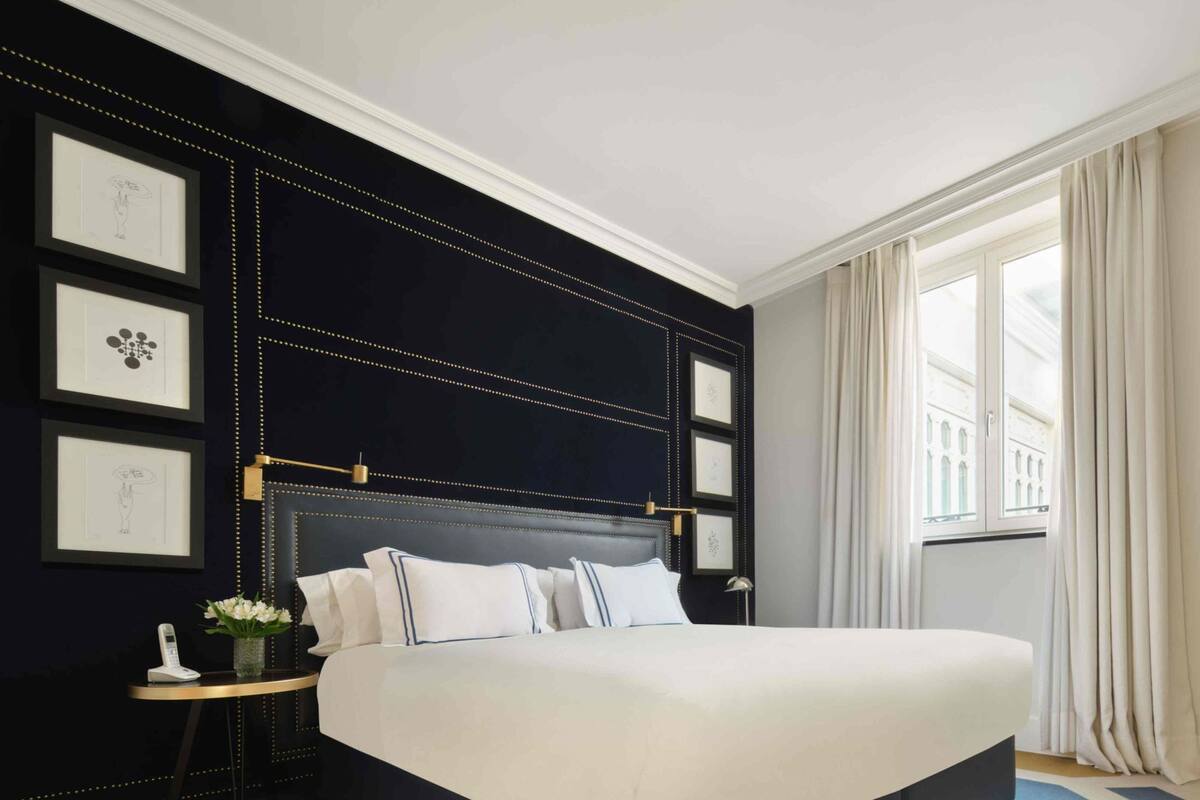Une chambre à coucher moderne avec un grand lit, une table de chevet avec une lampe et des œuvres d’art encadrées accrochées au mur.