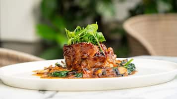 A plate of food with a meat dish, greens, and sauce on a white plate.