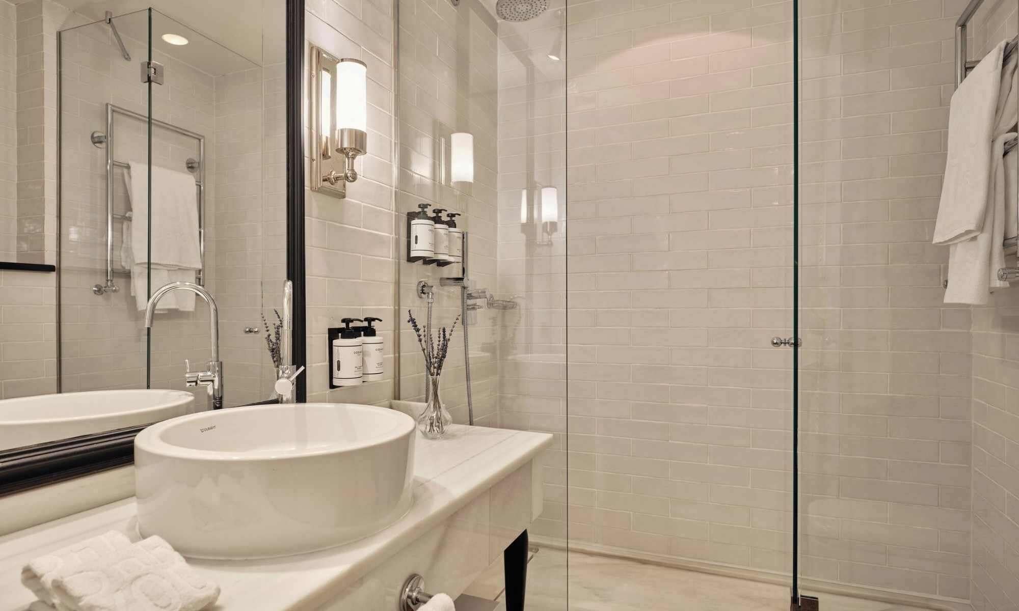 A modern bathroom with a glass-enclosed shower, a round sink, and a mirror.