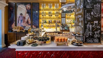 Eine Bar mit einer Auswahl an Getränken, einer Tafeln mit Speisenangeboten und einer Wand mit rotem Muster.