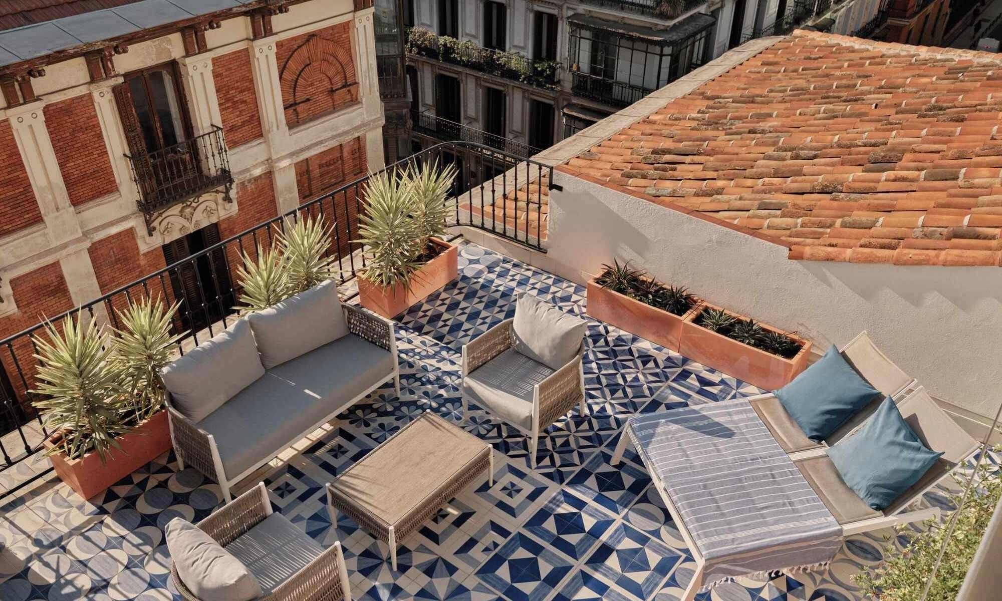 A rooftop terrace with a geometric patterned floor, outdoor furniture, and potted plants.