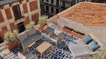 A rooftop terrace with a geometric patterned floor, outdoor furniture, and potted plants.