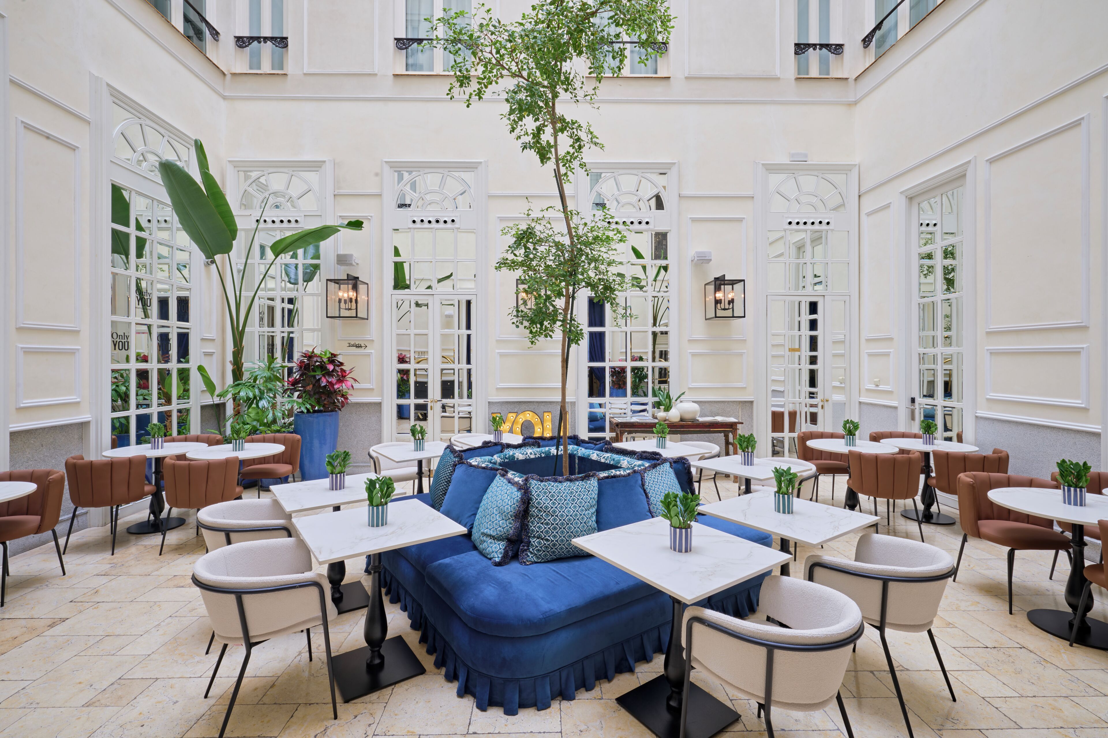 A spacious indoor seating area with a central blue sofa, multiple tables, and chairs arranged around it.