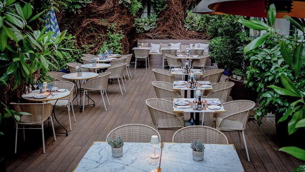 An outdoor patio with wicker furniture and marble-topped tables, surrounded by lush greenery. - Only YOU Boutique Hotel (Madrid)