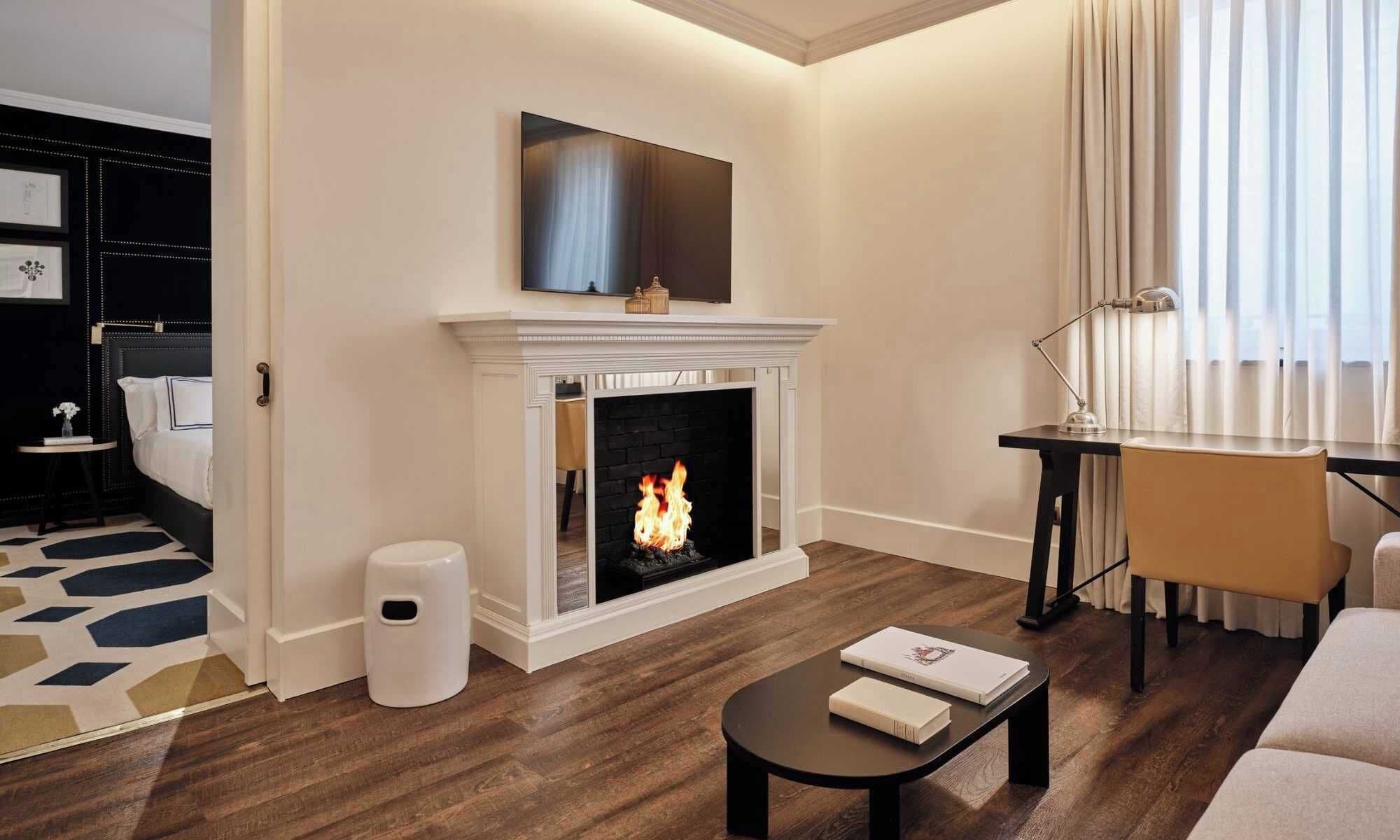 Una sala de estar moderna con chimenea, un televisor de pantalla plana encima, un escritorio con lámpara y un sofá.